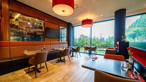 Un restaurante moderno con suelo de madera, asientos negros y rojos, y grandes ventanales que dan a zonas verdes.