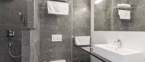 Un baño moderno con un lavamanos blanco, paredes de azulejos oscuros y un espejo sobre el lavamanos.