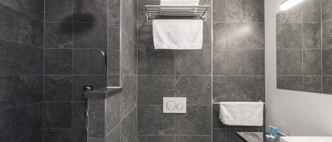 Un baño moderno con zócalos de mármol oscuro, ducha, inodoro y lavabo con espejo.
