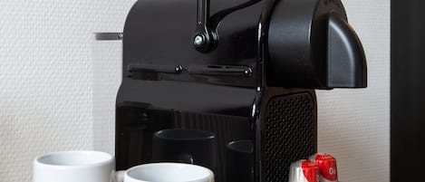 Una máquina de café espresso negra con dos tazas blancas que dicen 'Bastion Hotels.NL' sobre una superficie de madera.