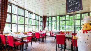 A restaurant with red chairs and tables, large windows, and a chef statue. - Bastion Hotel Heerlen (Heerlen)