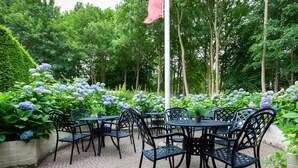 An outdoor patio with black metal tables and chairs, surrounded by lush greenery and hydrangea flowers. - Bastion Hotel Heerlen (Heerlen)