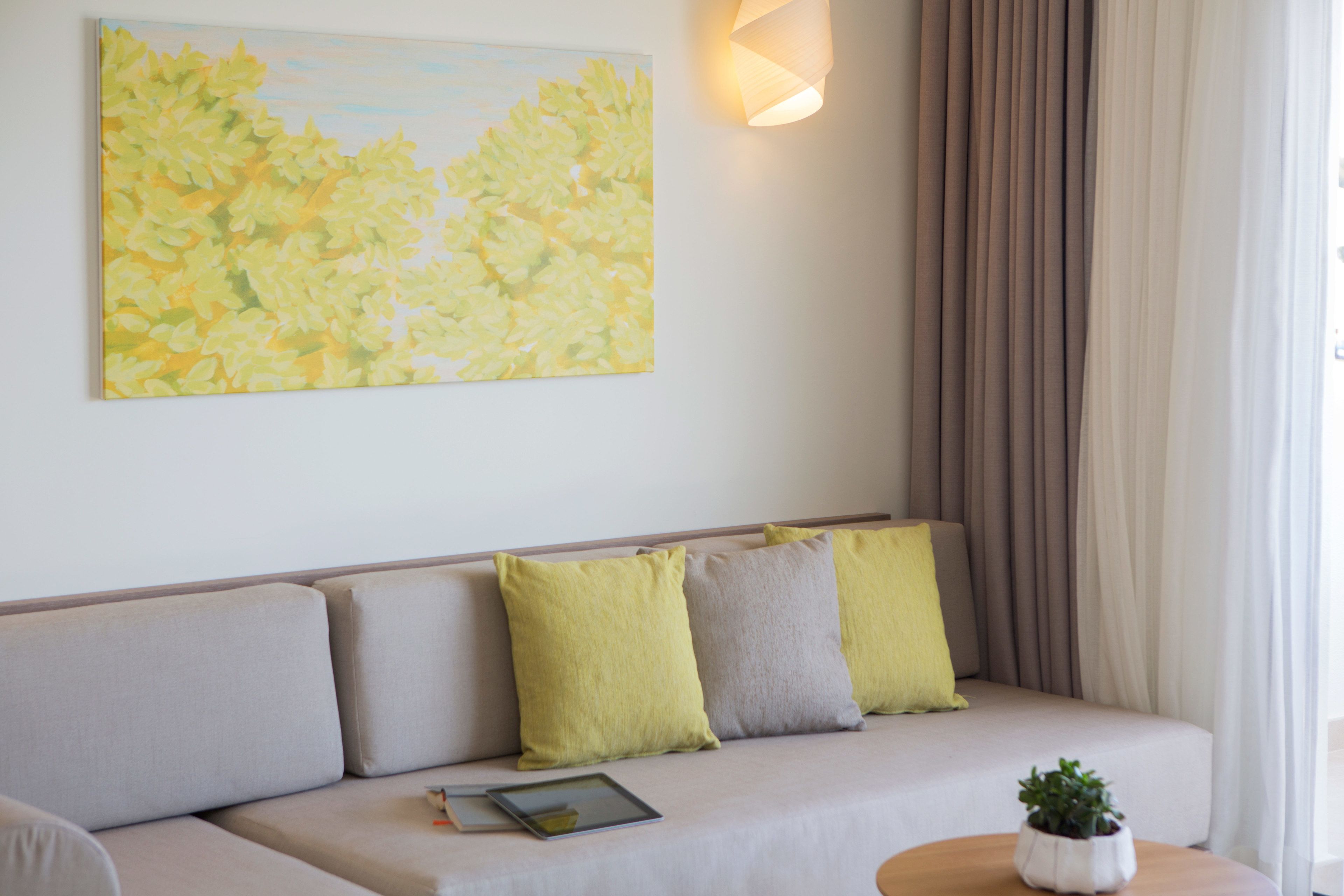 A modern living room with a beige sofa, a tablet on it, and a potted plant on a side table.