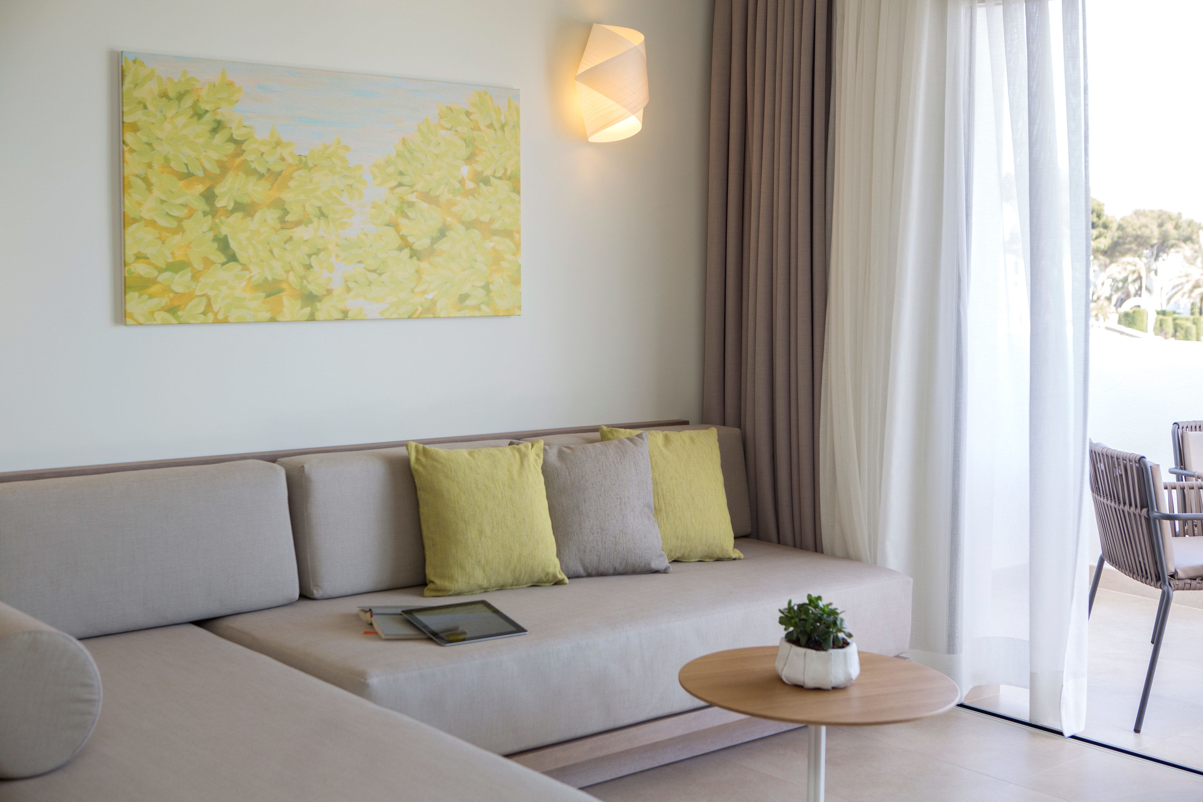 A modern living room with a sofa, cushions, a small table with a plant, a tablet, and a painting on the wall.