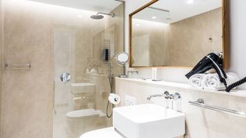 Un baño moderno con ducha de vidrio, lavamanos blanco y un espejo grande.