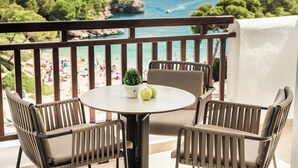 Un balcón con una mesa redonda y cuatro sillas, con vista a una playa con gente y vegetación.