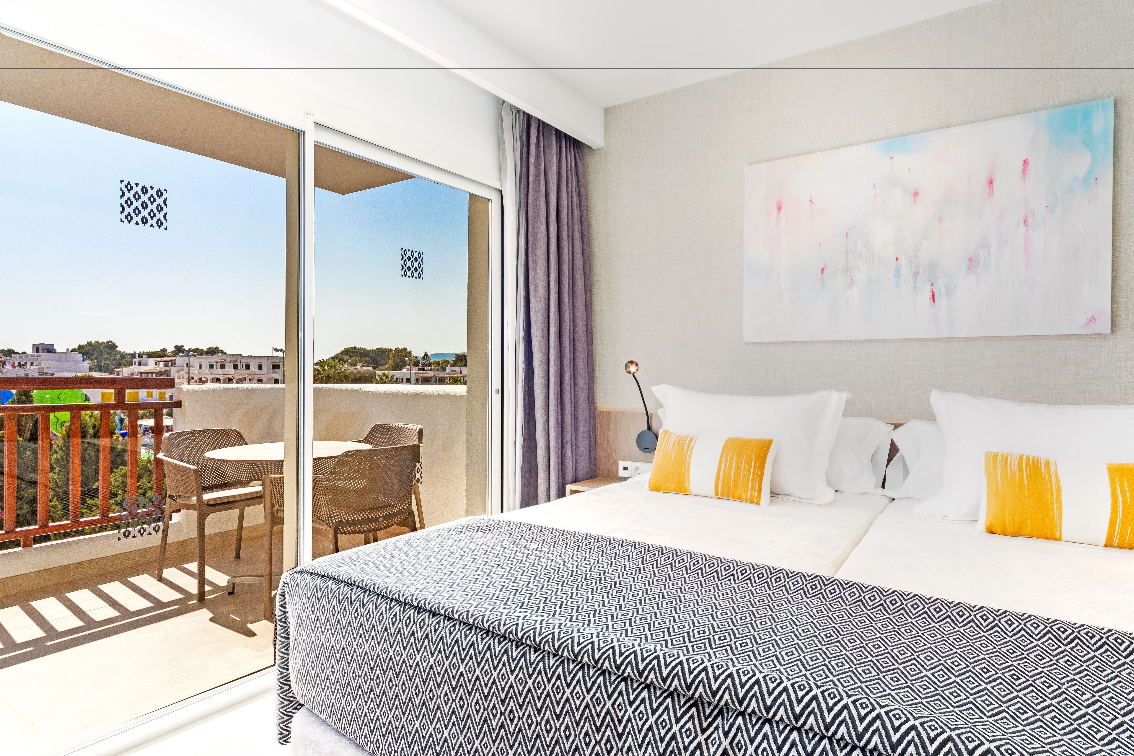 A hotel room with a balcony, a bed with patterned bedding, and a painting on the wall.