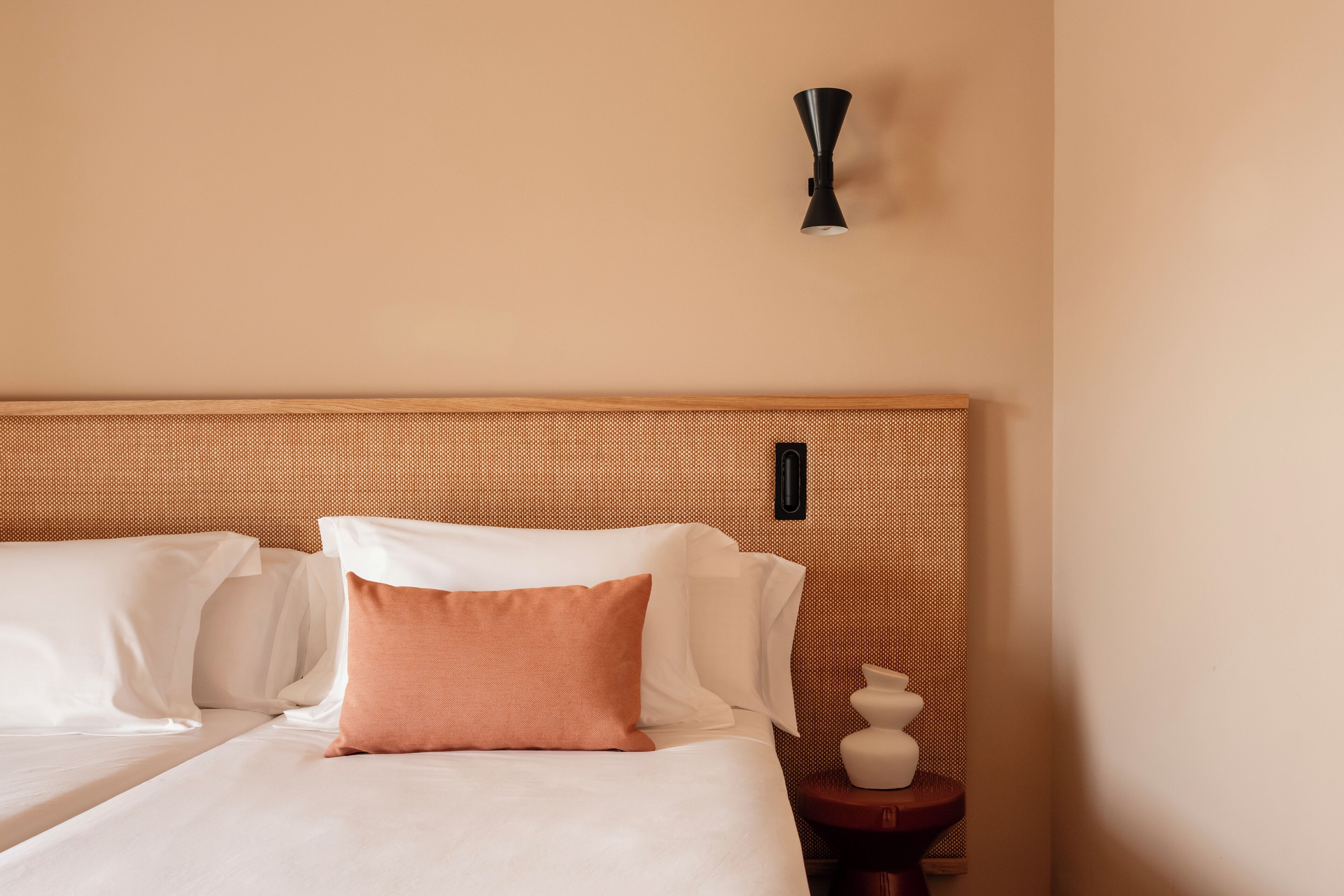 Una habitación de hotel con una cama grande, un cabecero de madera y una mesita de noche con un florero.