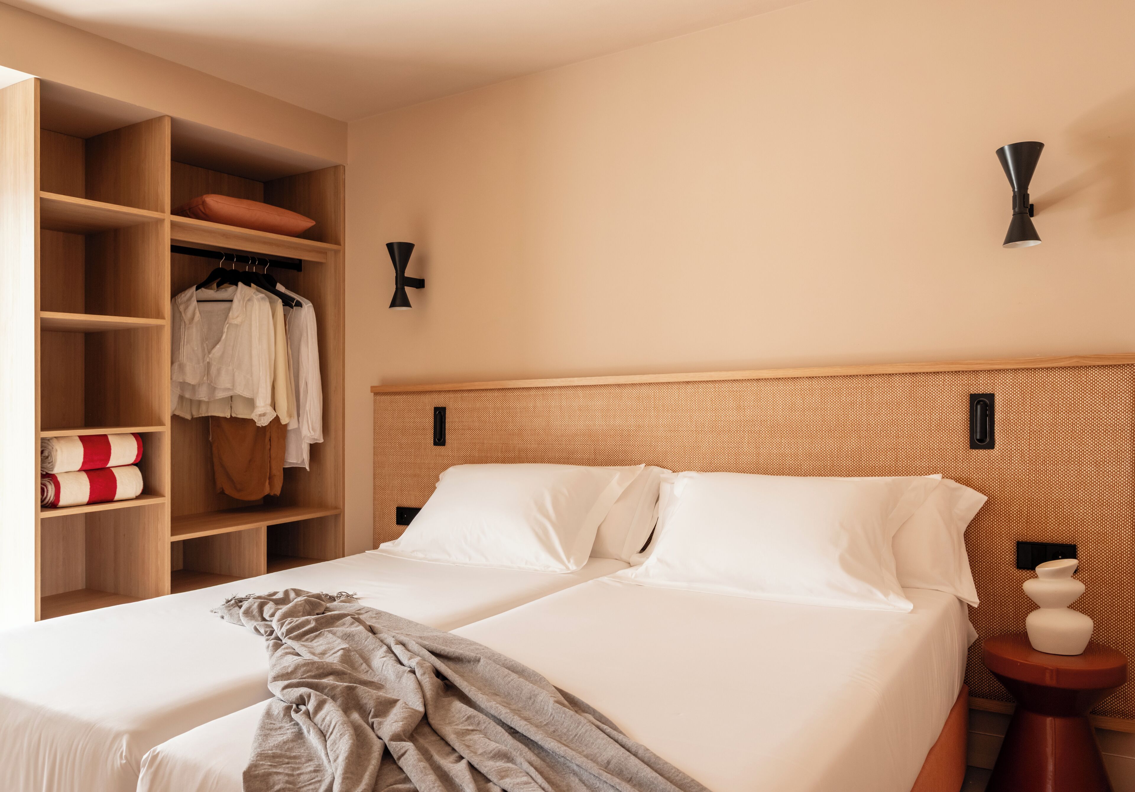Habitación de hotel con dos camas, un armario y una mesita de noche con un jarrón.