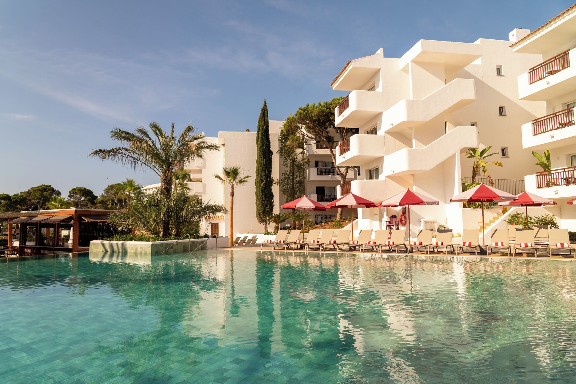 Zona de piscina amb aigua cristal·lina, gandules i para-sols.
