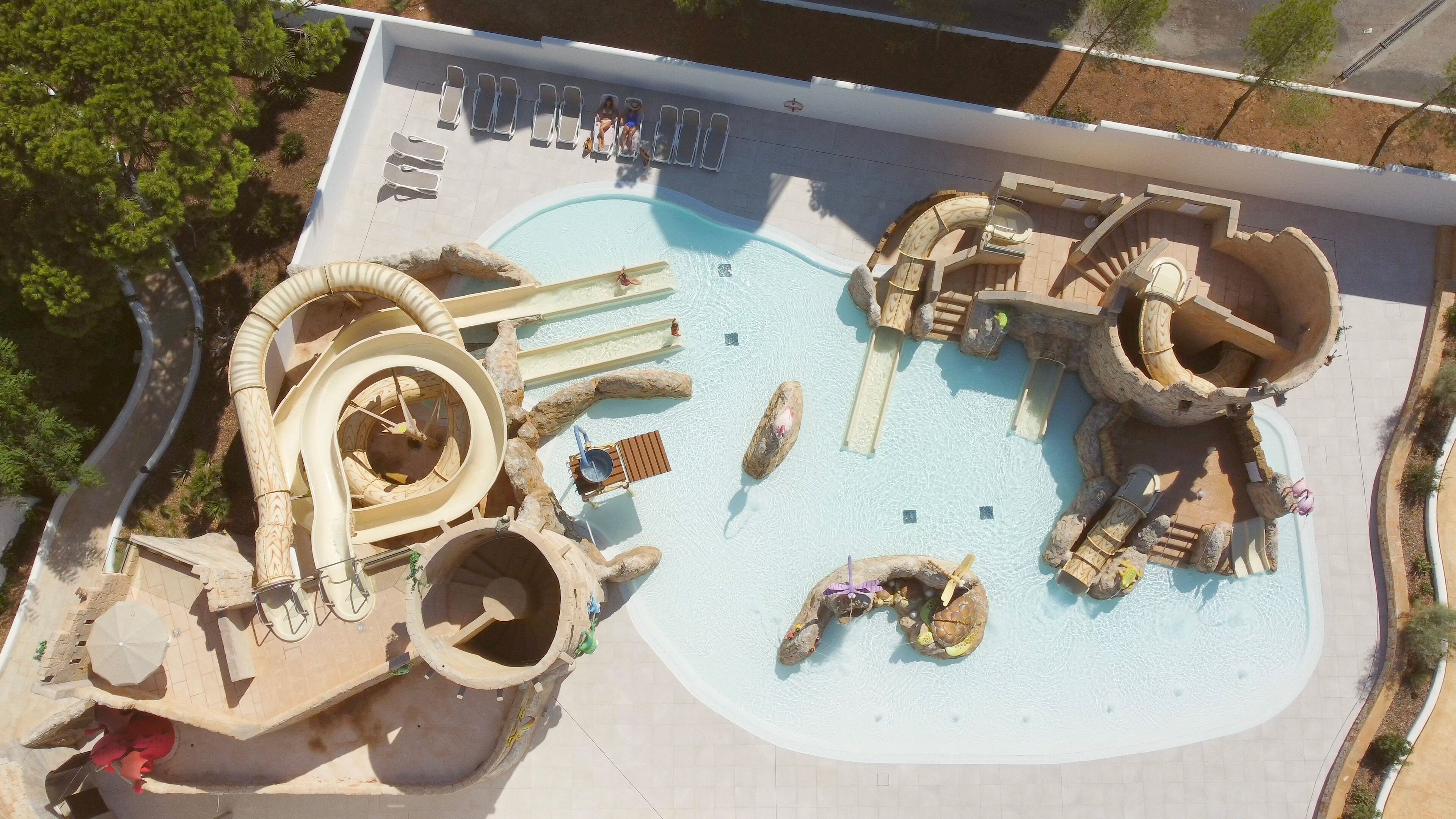 An aerial view of a water park with a large pool, slides, and various water features.