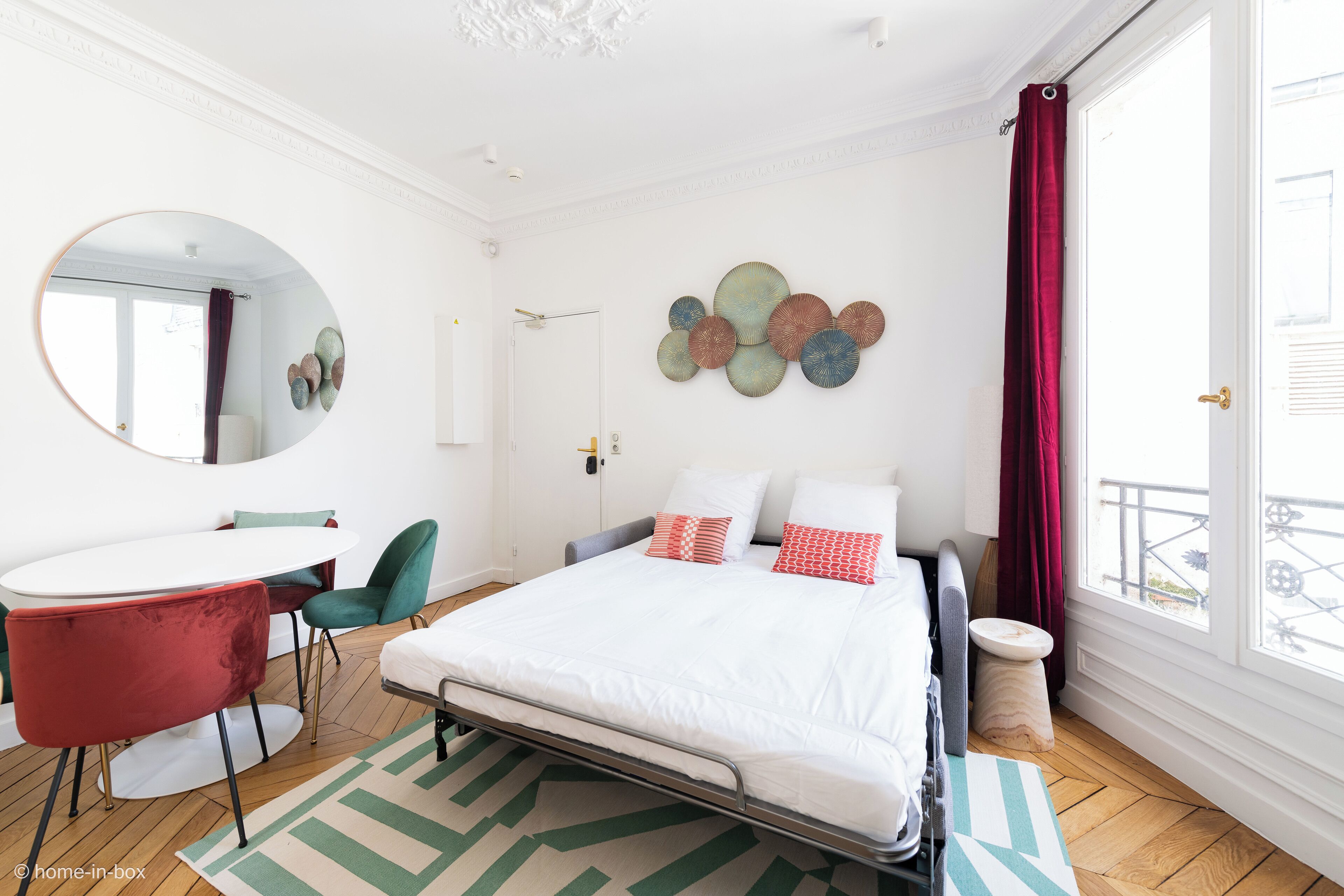 Un dormitorio moderno con cama, un espejo redondo, una mesa redonda y vistas al exterior.