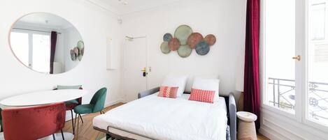 Un dormitorio moderno con cama, un espejo redondo, una mesa redonda y vistas al exterior.