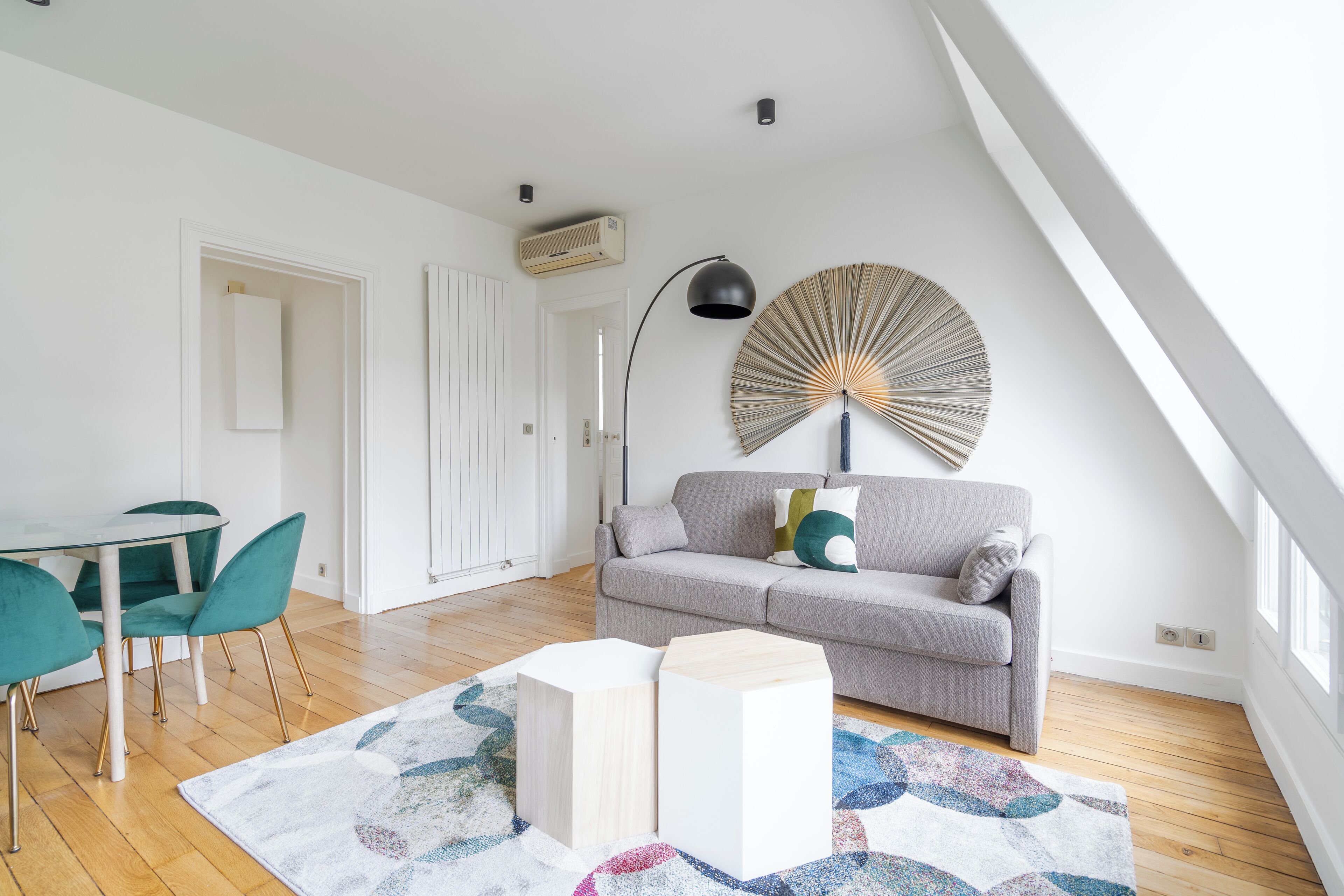 A modern living room with a grey sofa, teal chairs, a round wall decoration, and a patterned rug.