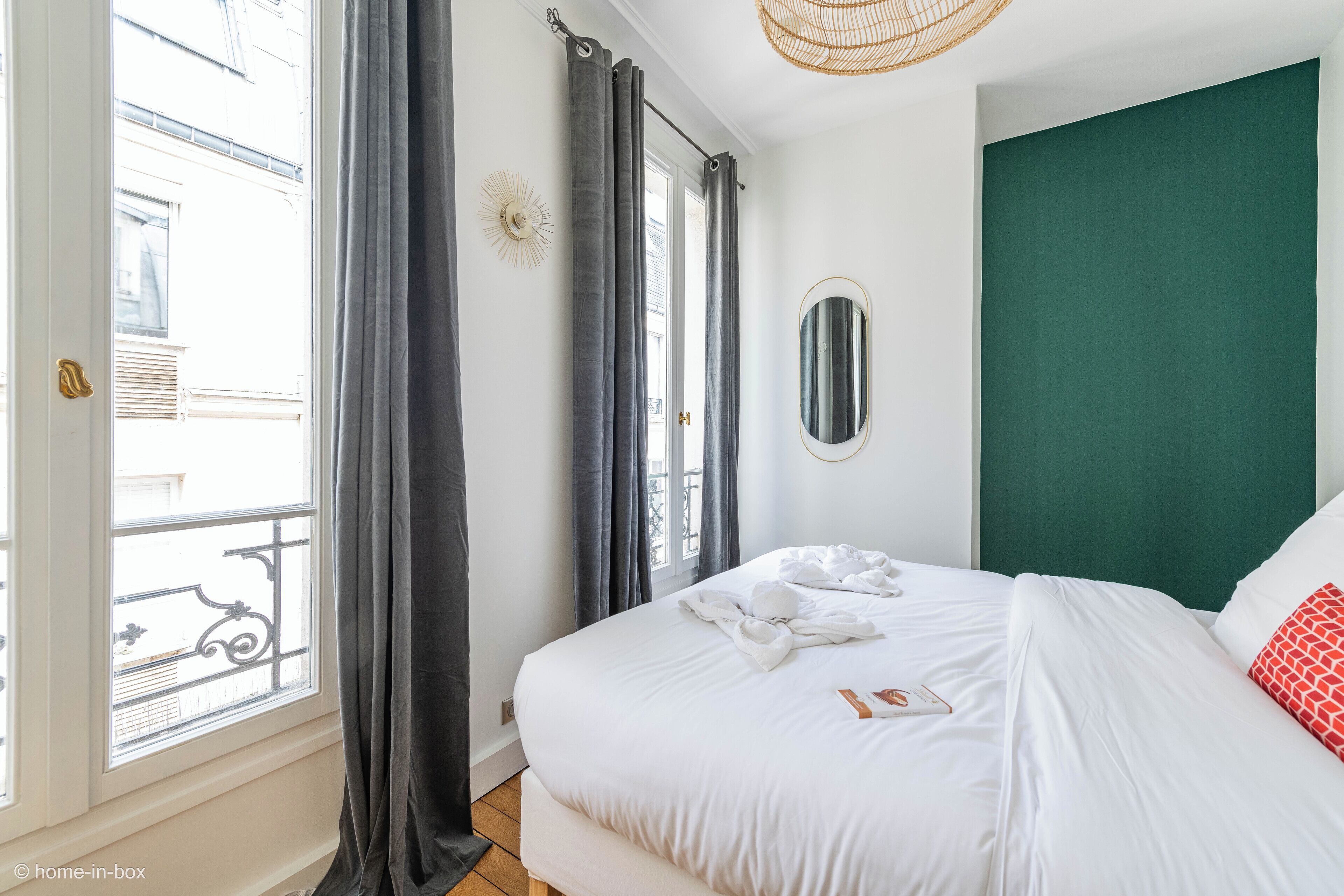 A bedroom with a large bed, a view of the outside balcony, and a green accent wall.