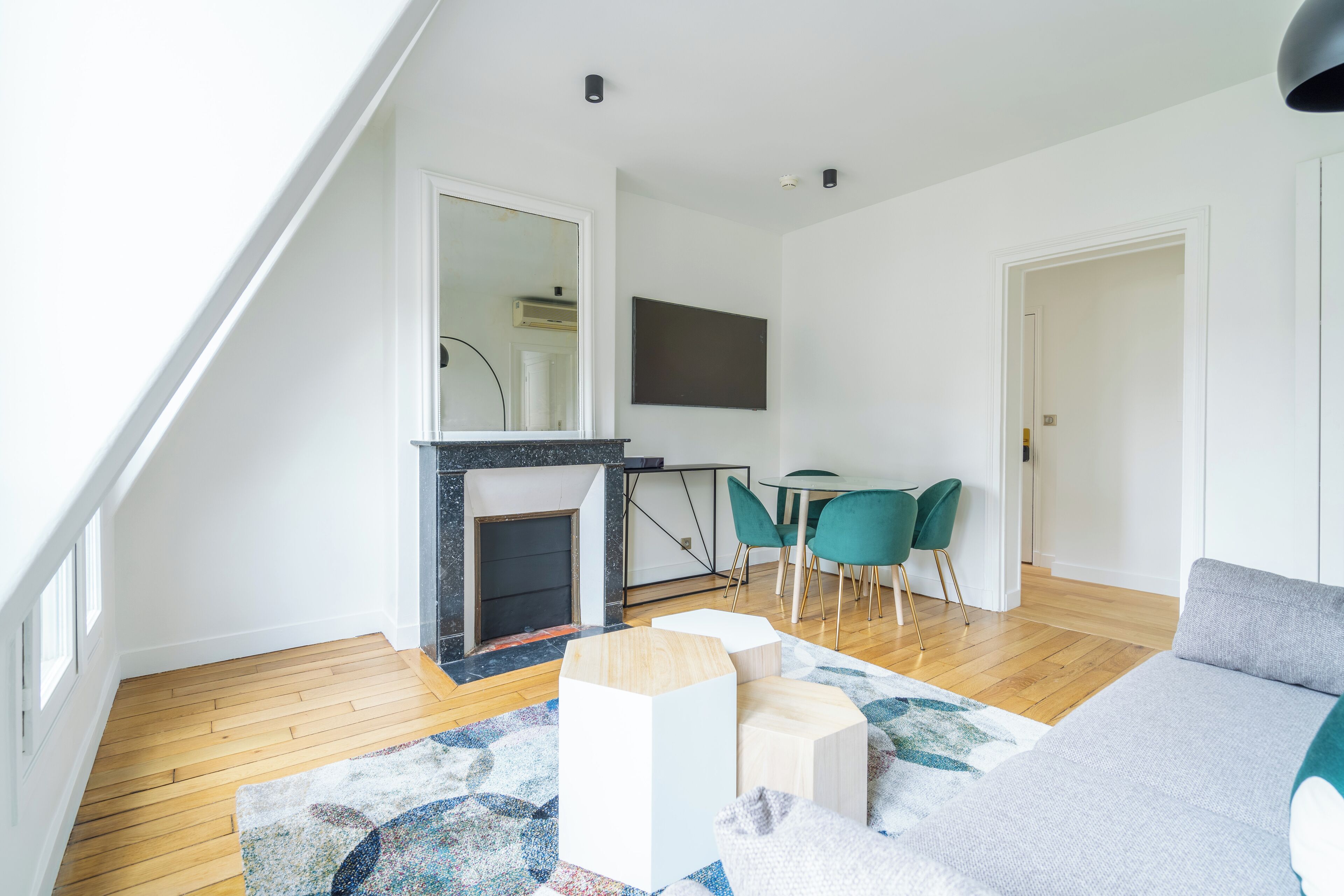 Uma sala de estar moderna com lareira, piso de madeira, um sofá e uma área de jantar com cadeiras.