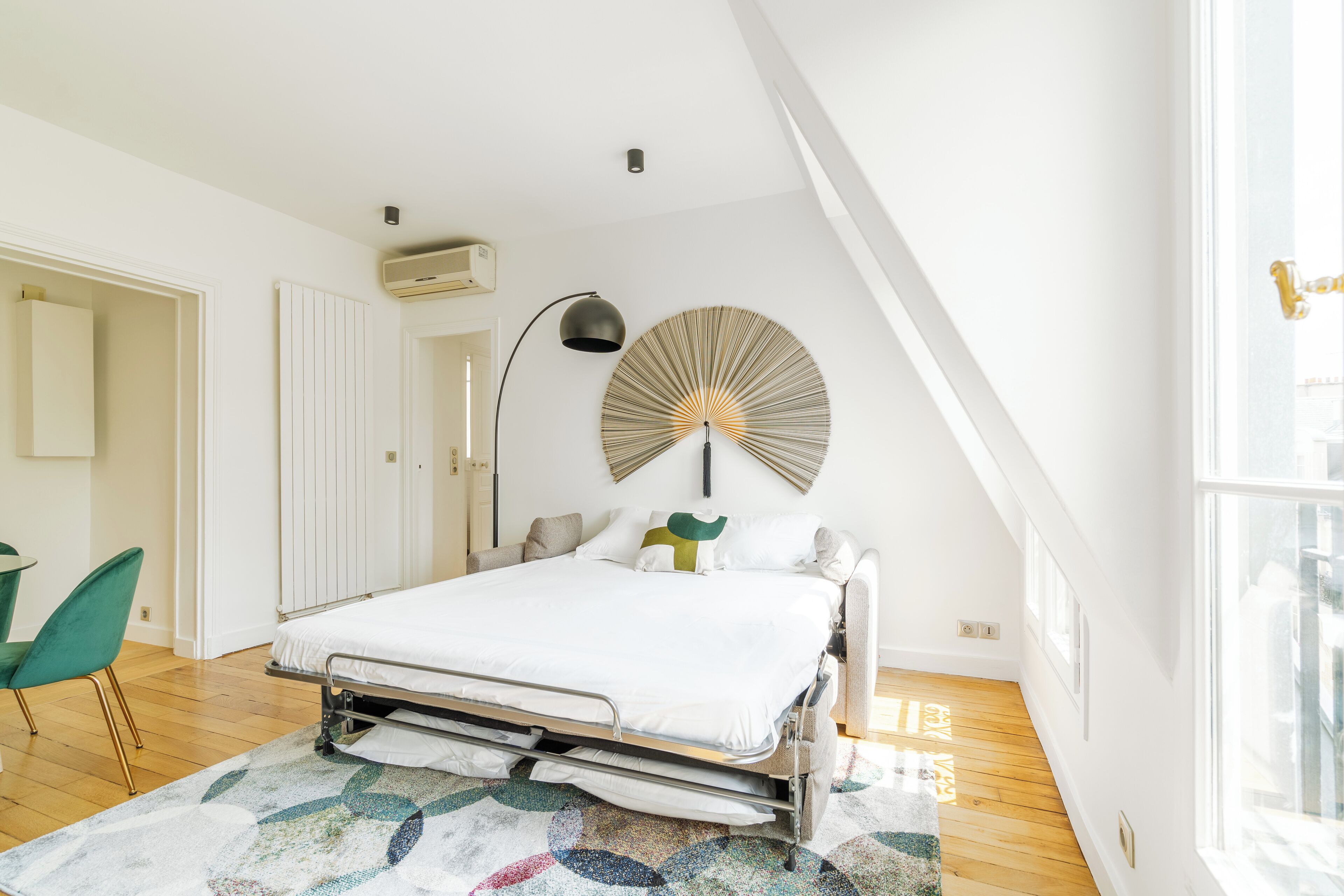 A modern bedroom with a bed, a bedside lamp, a radiator, and a window.