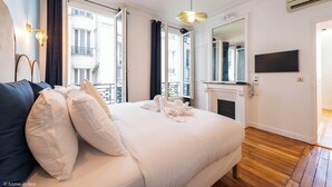 A bedroom with a large bed, a sofa, a fireplace, and a TV. - HotelHome Paris 16 (Paris)