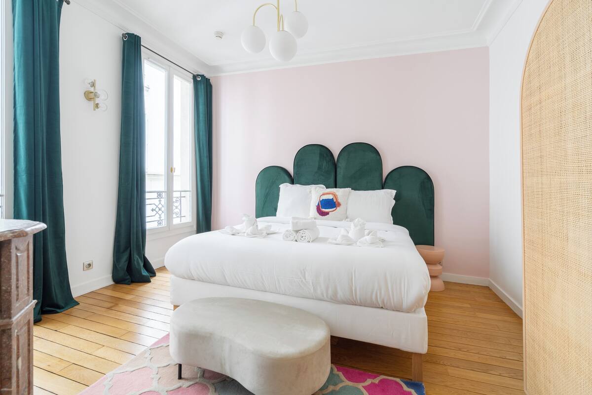A bedroom with a large bed, a bench, and a window with curtains.