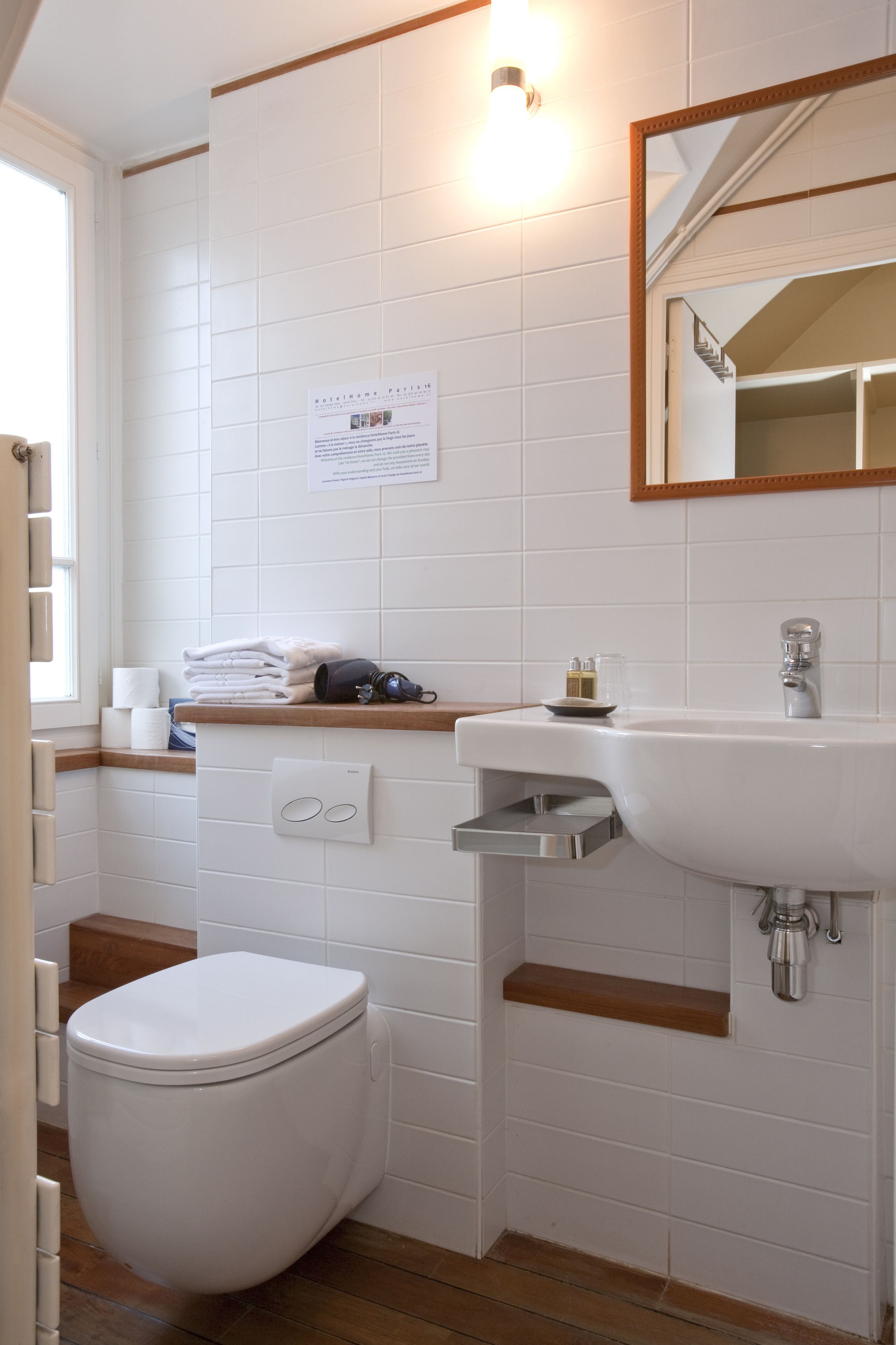 Ein Badezimmer mit einer weißen Toilette, einem Waschbecken und einem Spiegel. Handtücher und eine Seifenflasche befinden sich an einem Handtuchhalter.