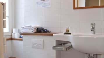 A bathroom with a white toilet, a sink, and a mirror. There is a towel rack with towels and a bottle of soap.