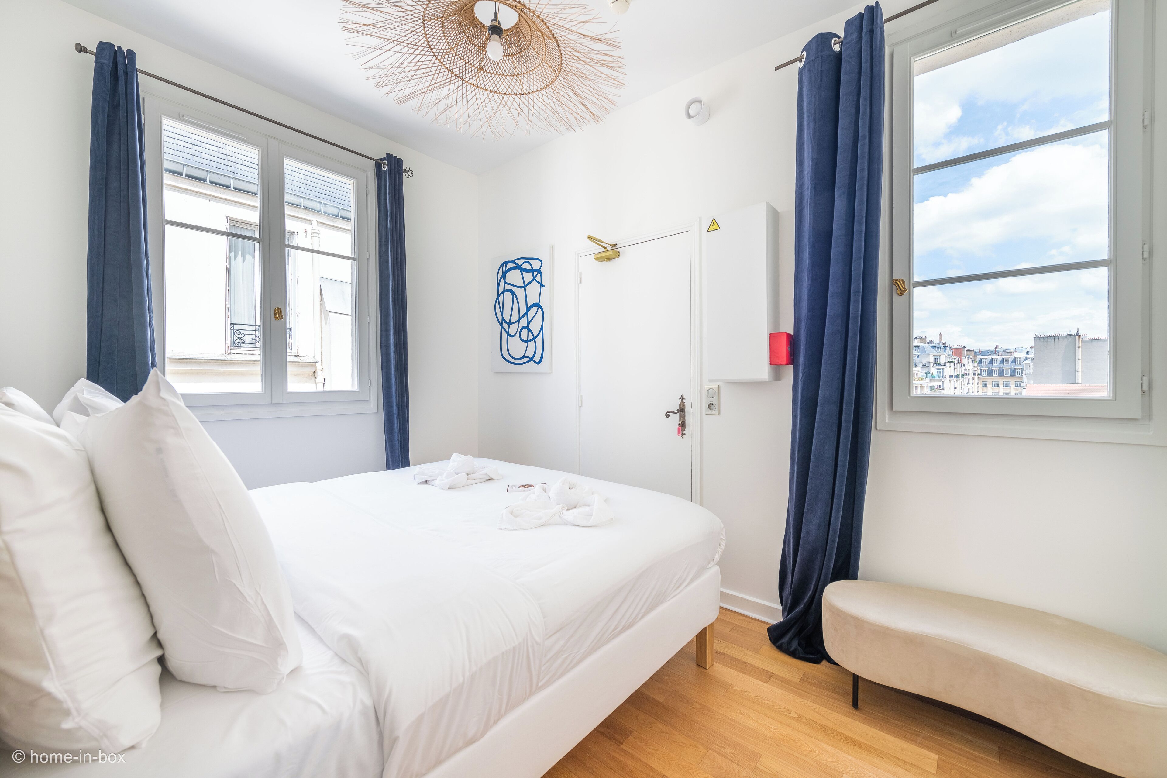 Ein modernes Schlafzimmer mit einem großen Bett, einer Bank und Blick auf die Stadt durch das Fenster.