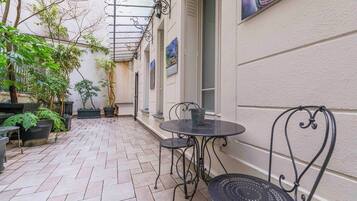 En overdækket terrasse med flisegulv, metalstole og krukker med planter.