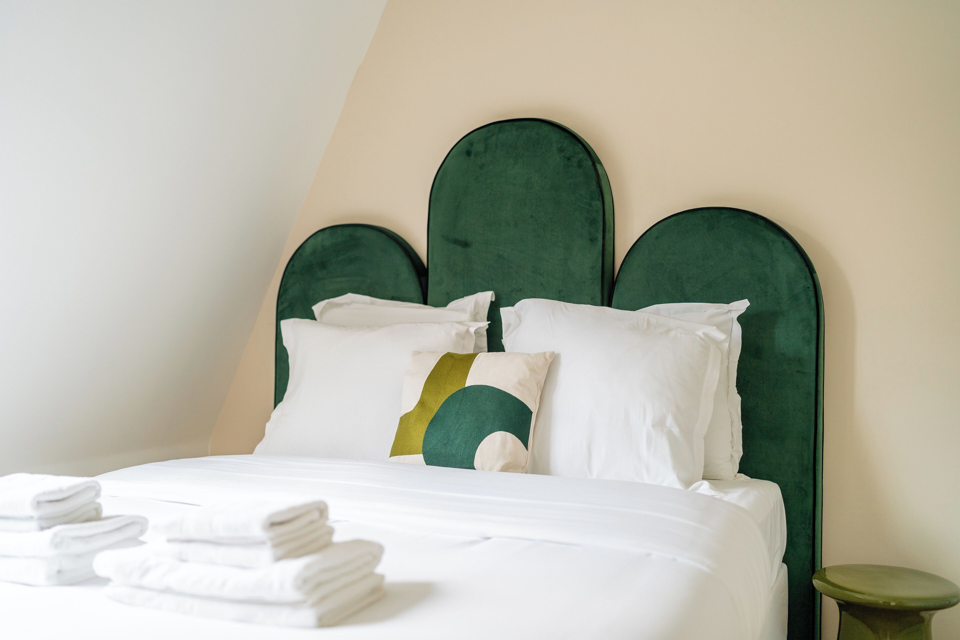 Een keurig opgemaakt bed met witte lakens en een groen bekleden hoofdeinde.