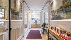 A hallway with a red carpet, a wooden bench with books, and a glass door leading to a room. - HotelHome Paris 16 (Paris)