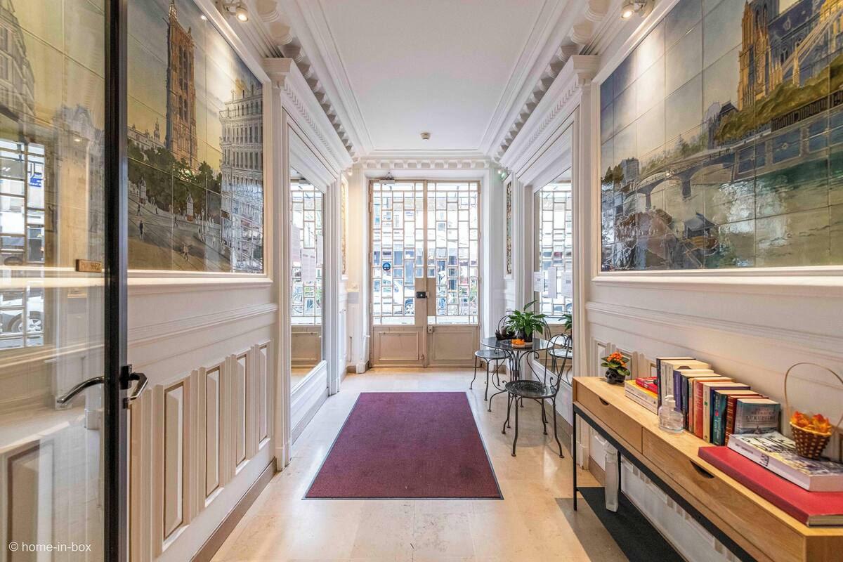 A hallway with a red carpet, a wooden bench with books, and a glass door leading to a room.