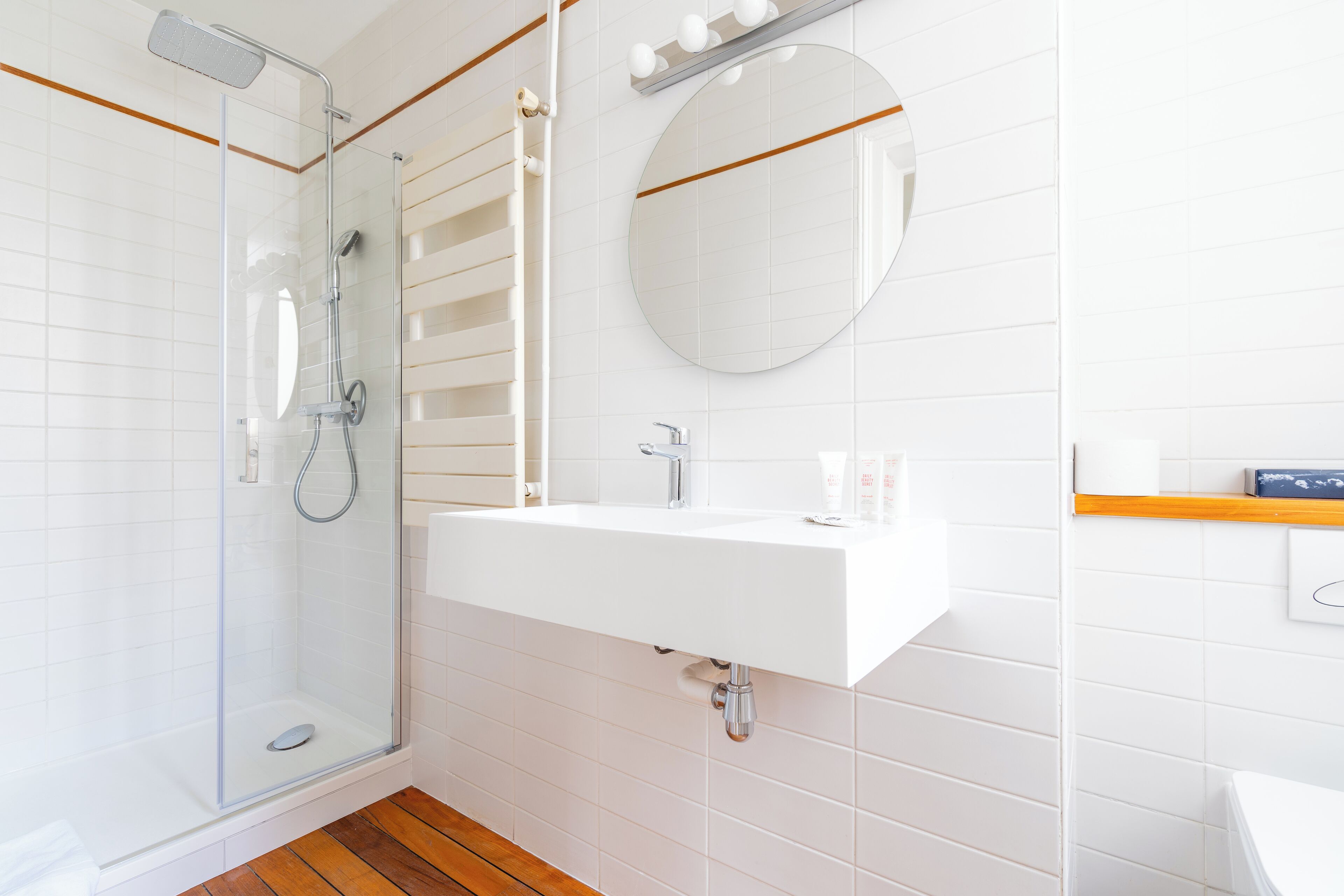 Ein modernes Badezimmer mit einer Glaskabine zur Dusche, einem weißen Waschbecken und einem runden Spiegel.