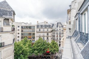 A narrow street with buildings on either side, trees in the foreground, and a red car parked on the sidewalk. - HotelHome Paris 16 (Paris)