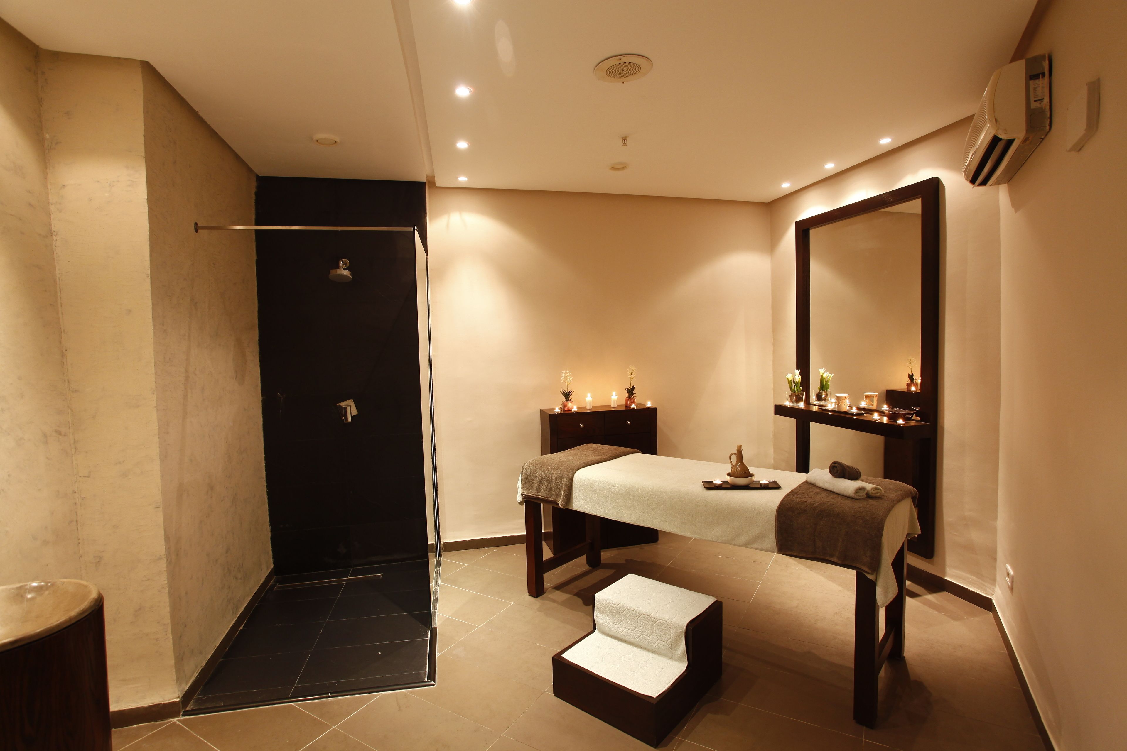 A modern bathroom with a walk-in shower, a vanity with a mirror, and a massage table.