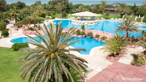A resort with a large central pool, surrounded by palm trees and a view of the sea. - Regency Tunis Hotel (La Marsa)