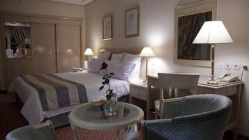 Habitación de hotel con cama, dos lámparas de noche, escritorio con teléfono, una silla y una pequeña mesa con un jarrón.