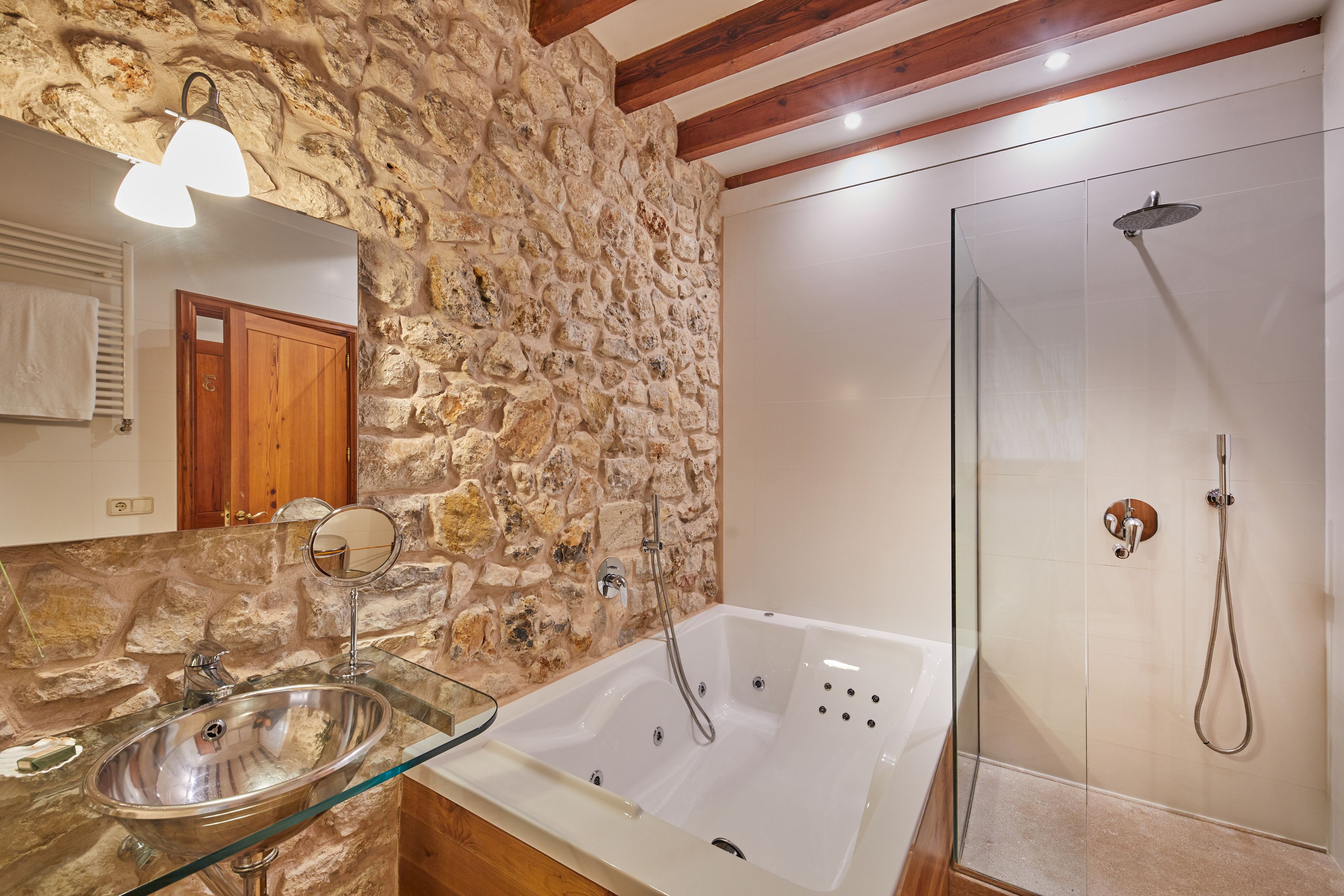 Une salle de bain avec un mur en pierre, un lavabo en verre, une baignoire et une douche.