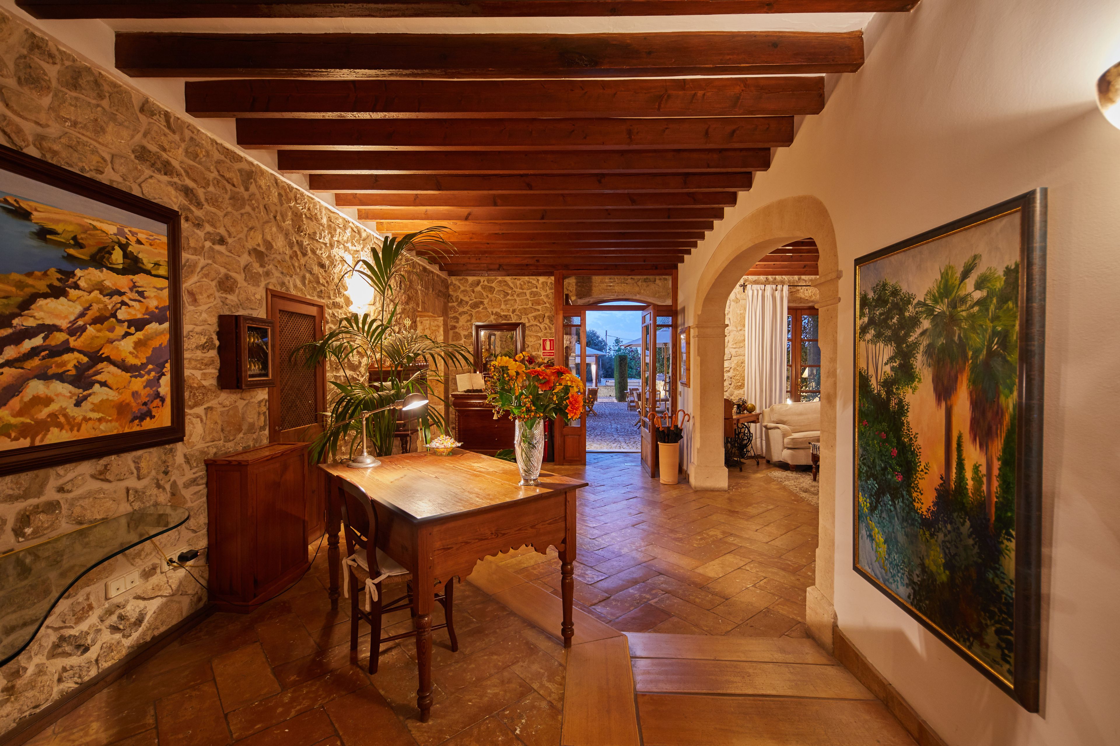 Un pasillo de paredes de piedra con vigas de madera, una mesa de comedor con sillas y un jarrón de flores.