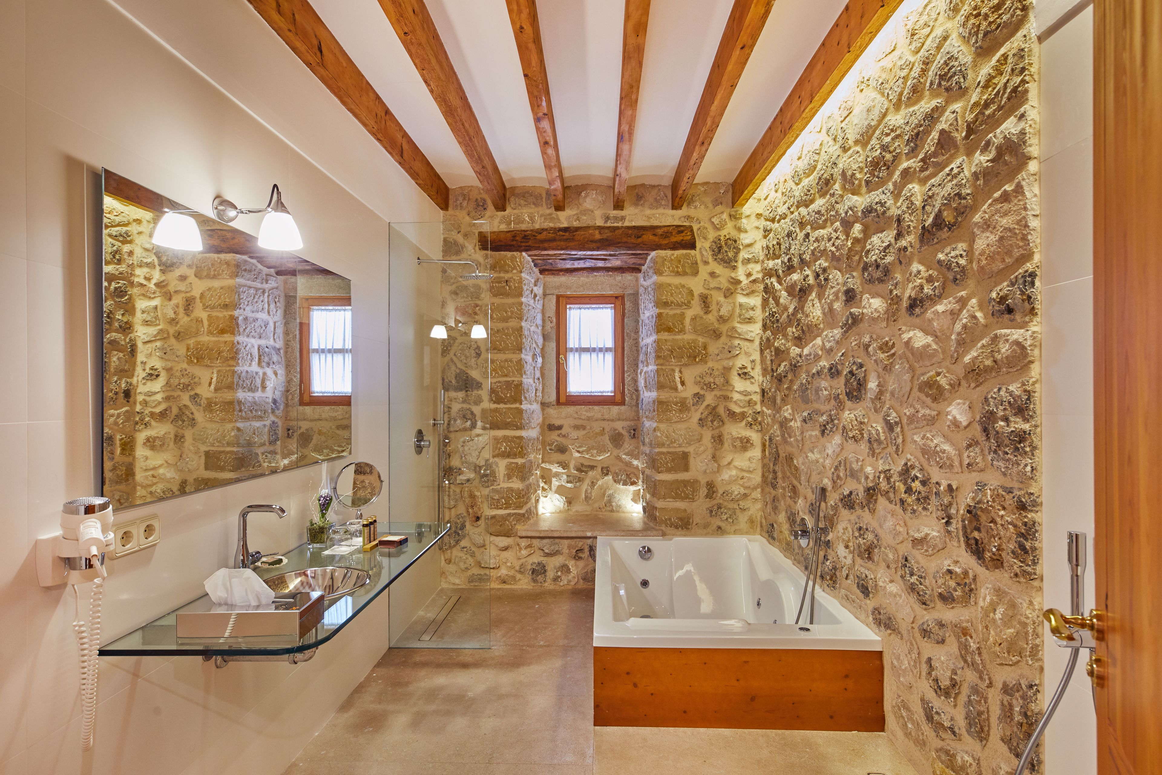 Un baño con pared de piedra, cabina de ducha de vidrio, bañera y techo de madera.