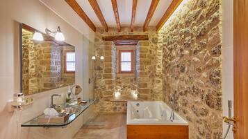 Un baño con pared de piedra, cabina de ducha de vidrio, bañera y techo de madera.