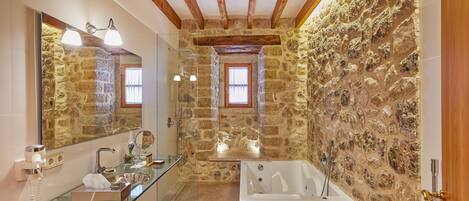 Un baño con pared de piedra, cabina de ducha de vidrio, bañera y techo de madera.