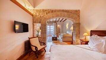 Un dormitorio con un arco de piedra, una cama, una silla, un televisor y vista a otra habitación.