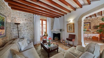 A cozy living room with stone walls, wooden beams, a fireplace, and comfortable seating.