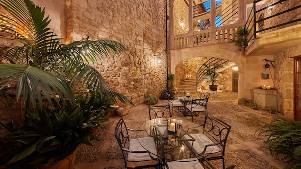An indoor courtyard with stone walls, a glass table with chairs, and potted plants. - Cas Comte Suites & Spa - Adults Only (Lloseta)