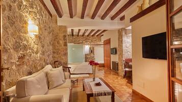 Una habitación de hotel acogedora con pared de piedra, techo de madera, cama, sofá, televisor y zona de comedor.