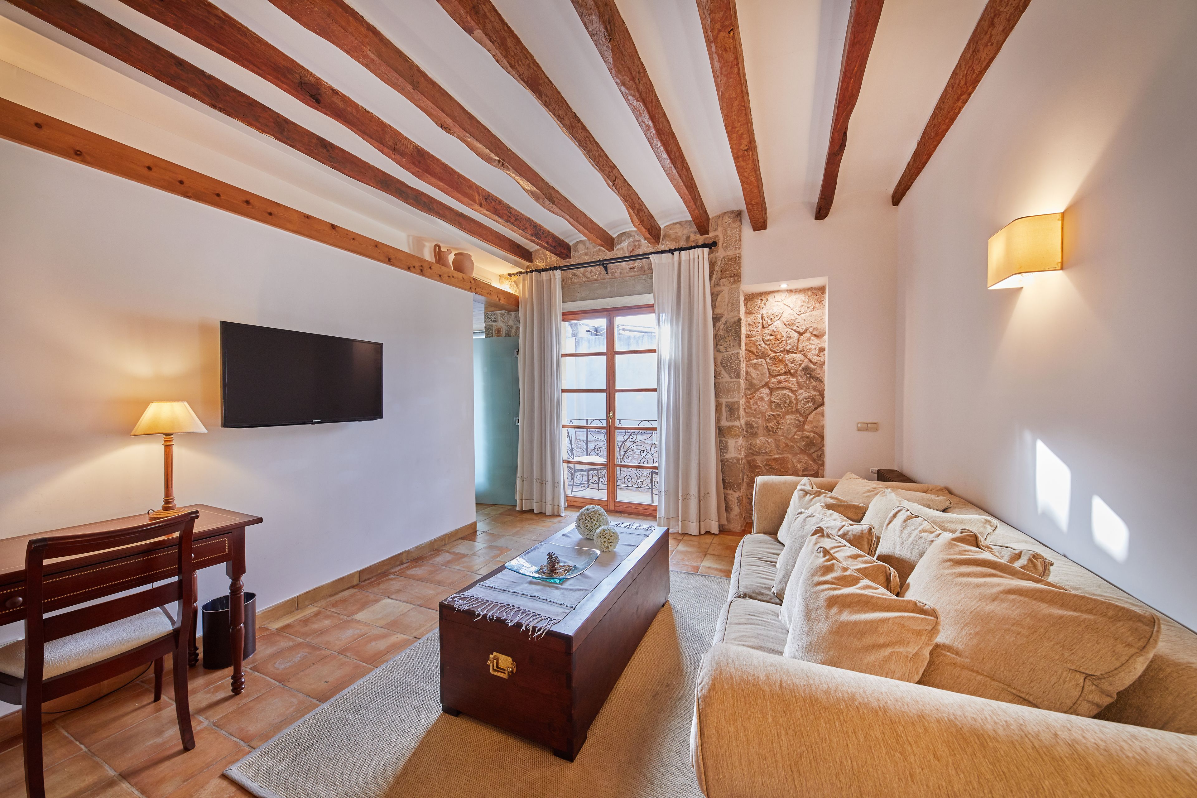 A living room with a wooden ceiling, a TV, a sofa, and a table with a lamp.