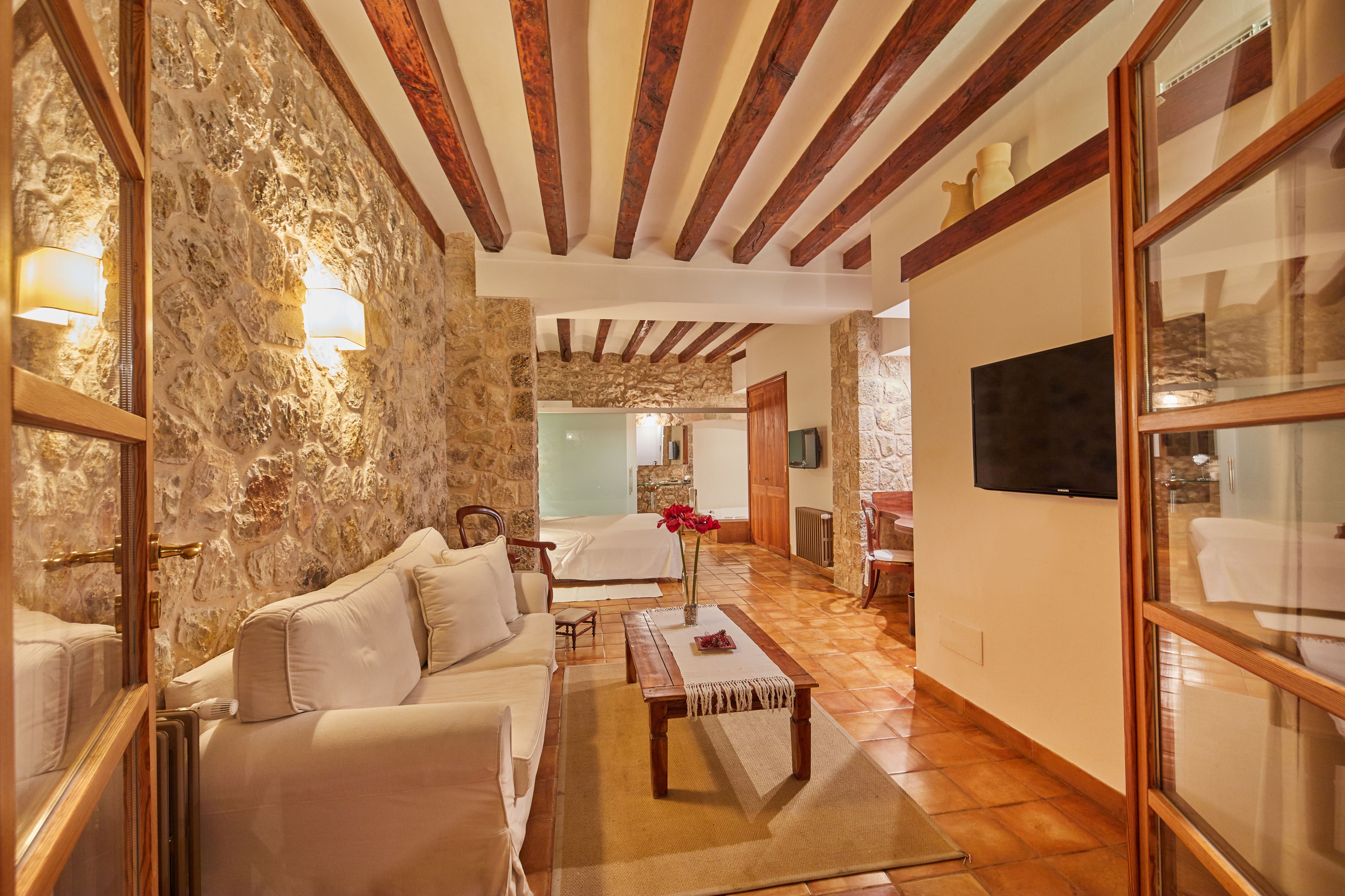 Una sala de estar acogedora con una pared de piedra, vigas de madera, un sofá, una mesa de centro y un televisor fijado a la pared.