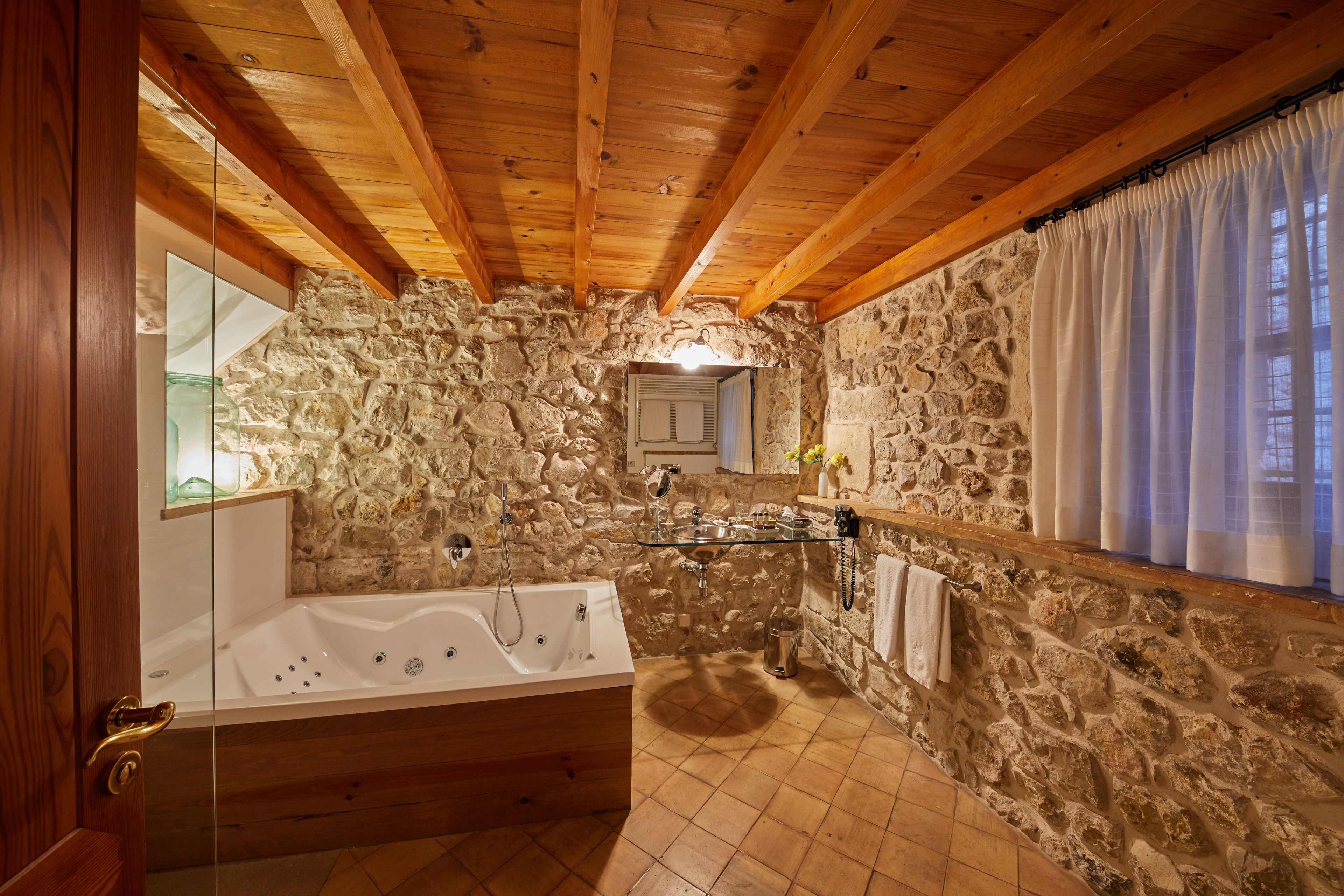 A stone-walled bathroom with a wooden ceiling, a bathtub, and a glass shower enclosure.