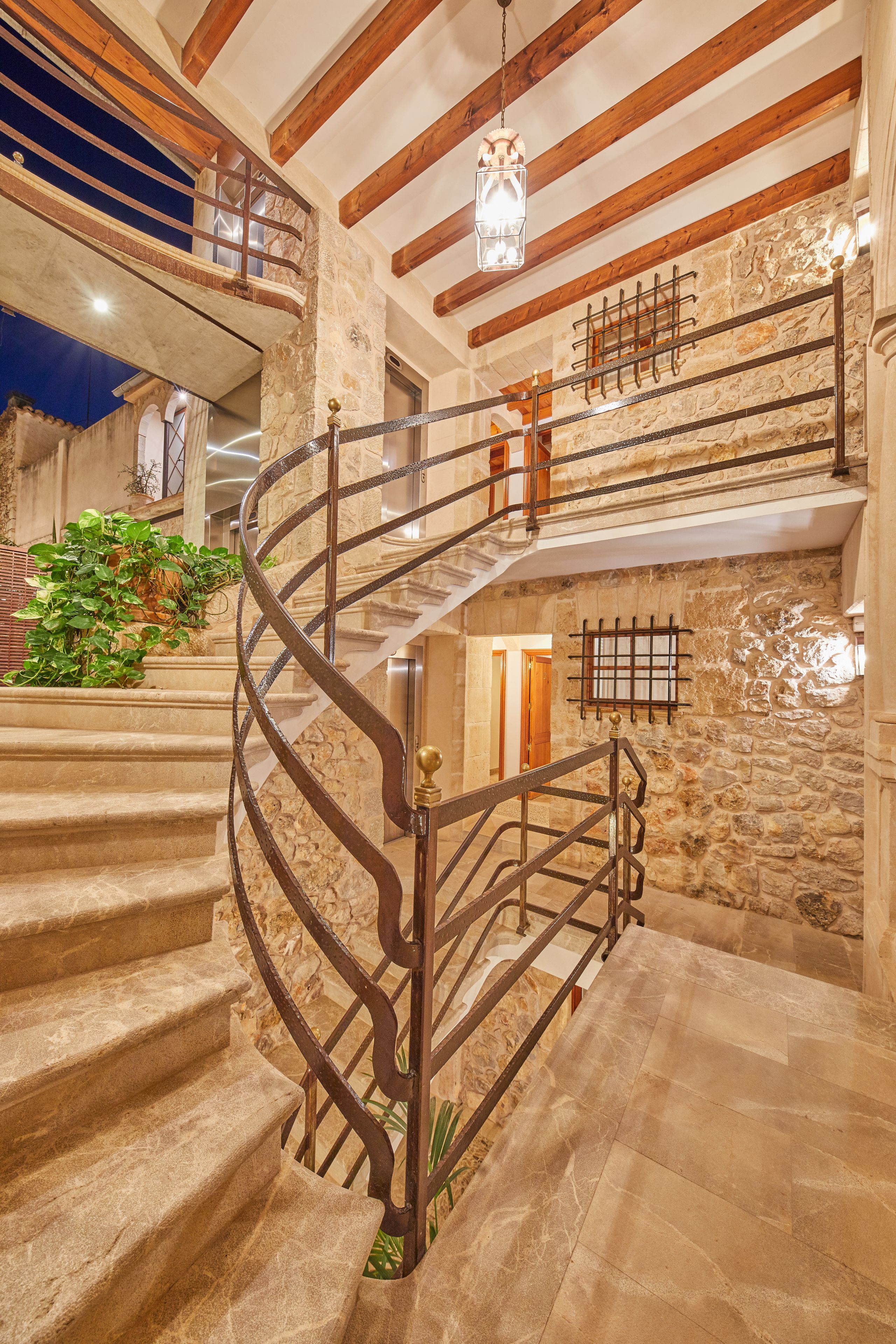 Una escalera de caracol con paredes de piedra y vigas de madera, que conduce a un nivel superior con un balcón.