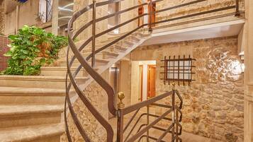 Una escalera de caracol con paredes de piedra y vigas de madera, que conduce a un nivel superior con un balcón.
