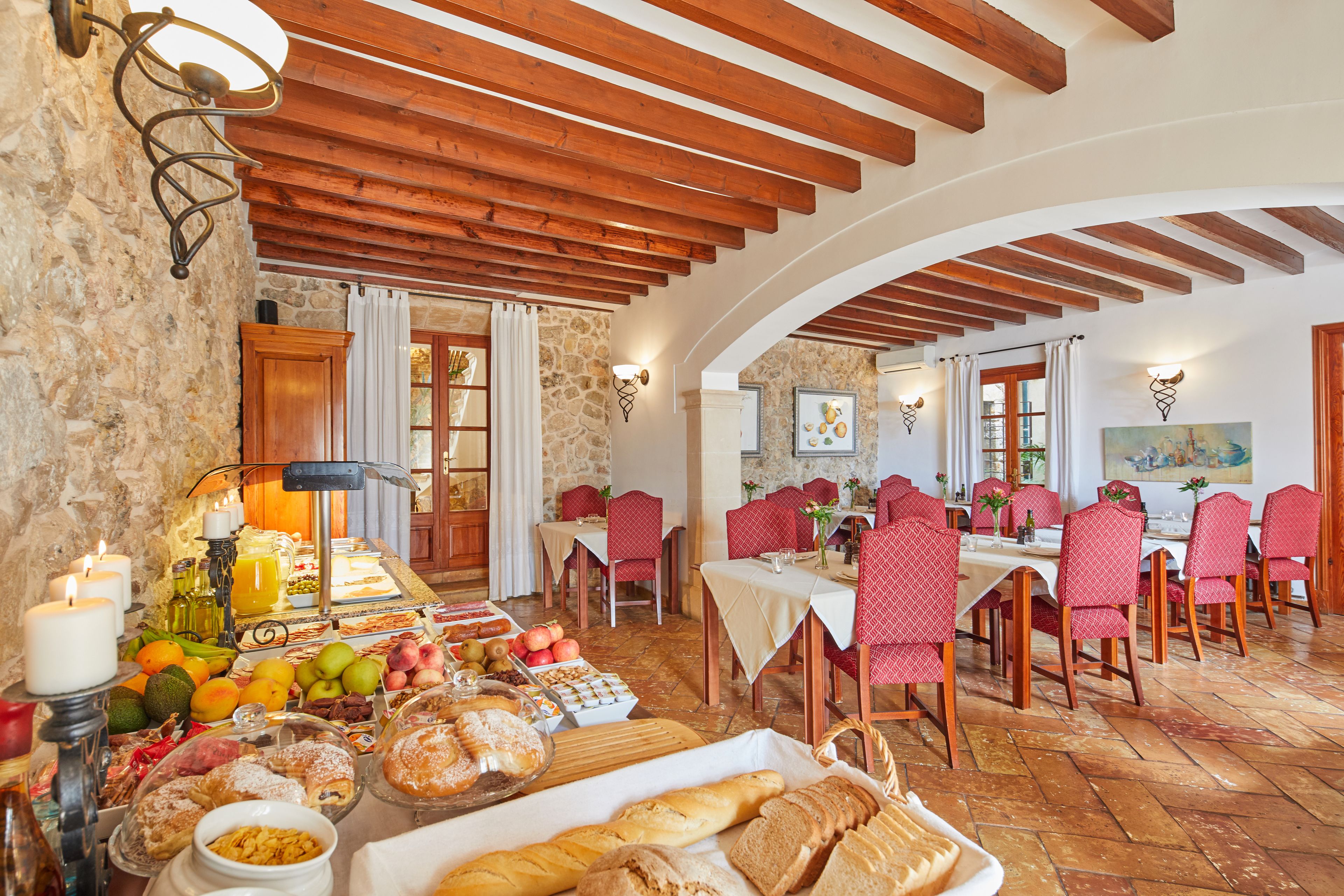 A dining area with a stone wall, wooden beams, and red upholstered chairs.